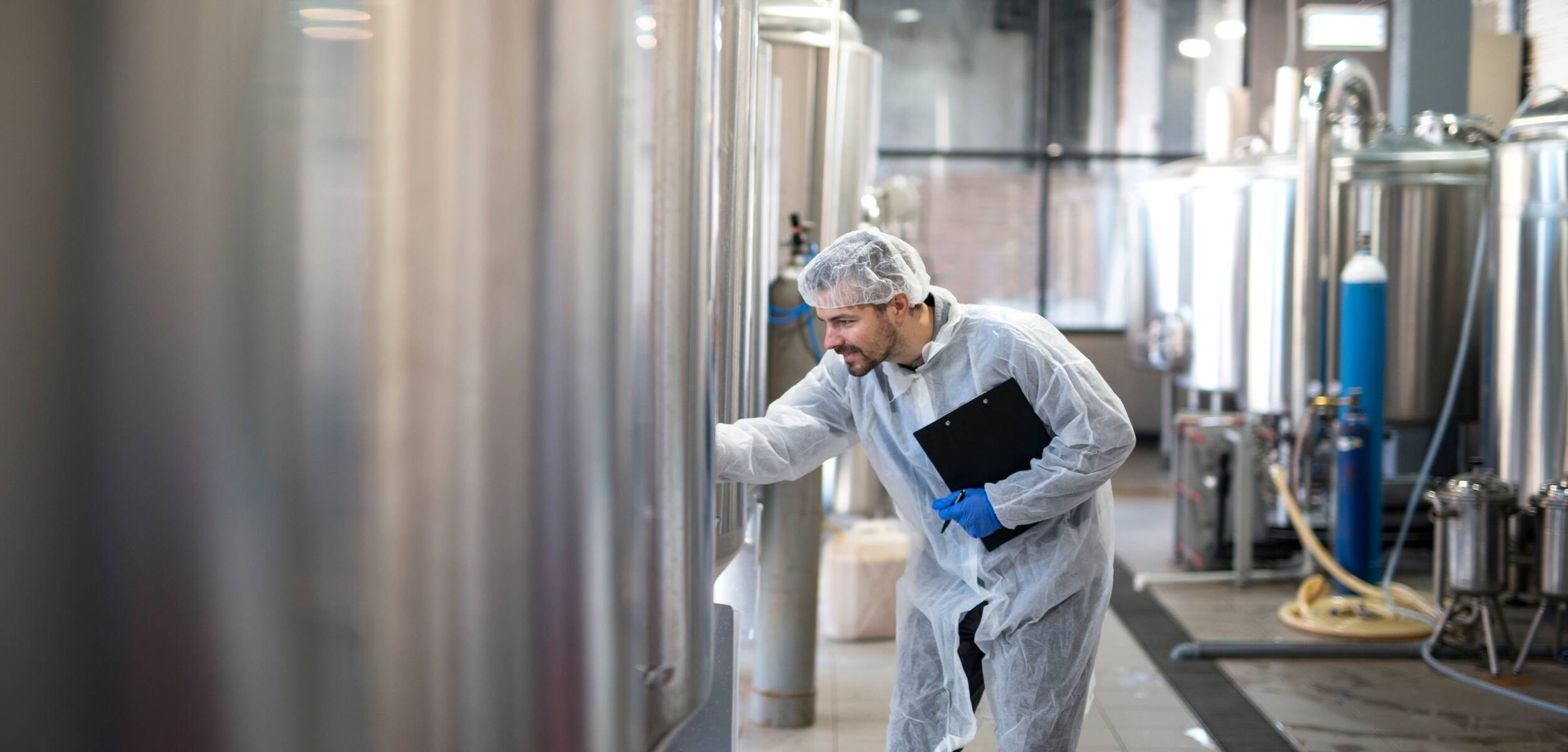 Un homme en combinaison blanc contrôle une cuve dans une usine