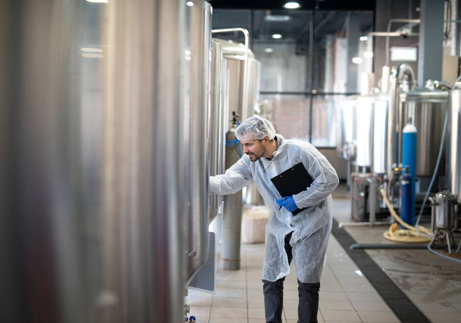 Un homme en combinaison blanc contrôle une cuve dans une usine